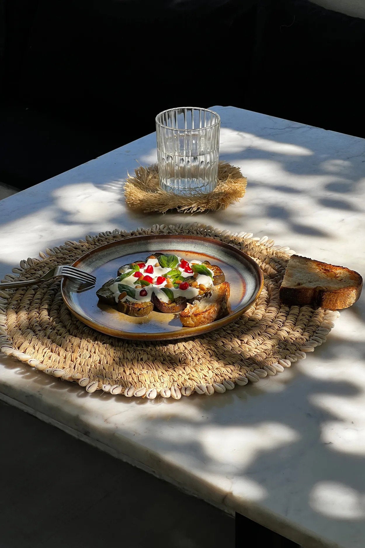 Woven raffia placemat with shells, ideal for protecting surfaces while enhancing everyday meals with boho style.
