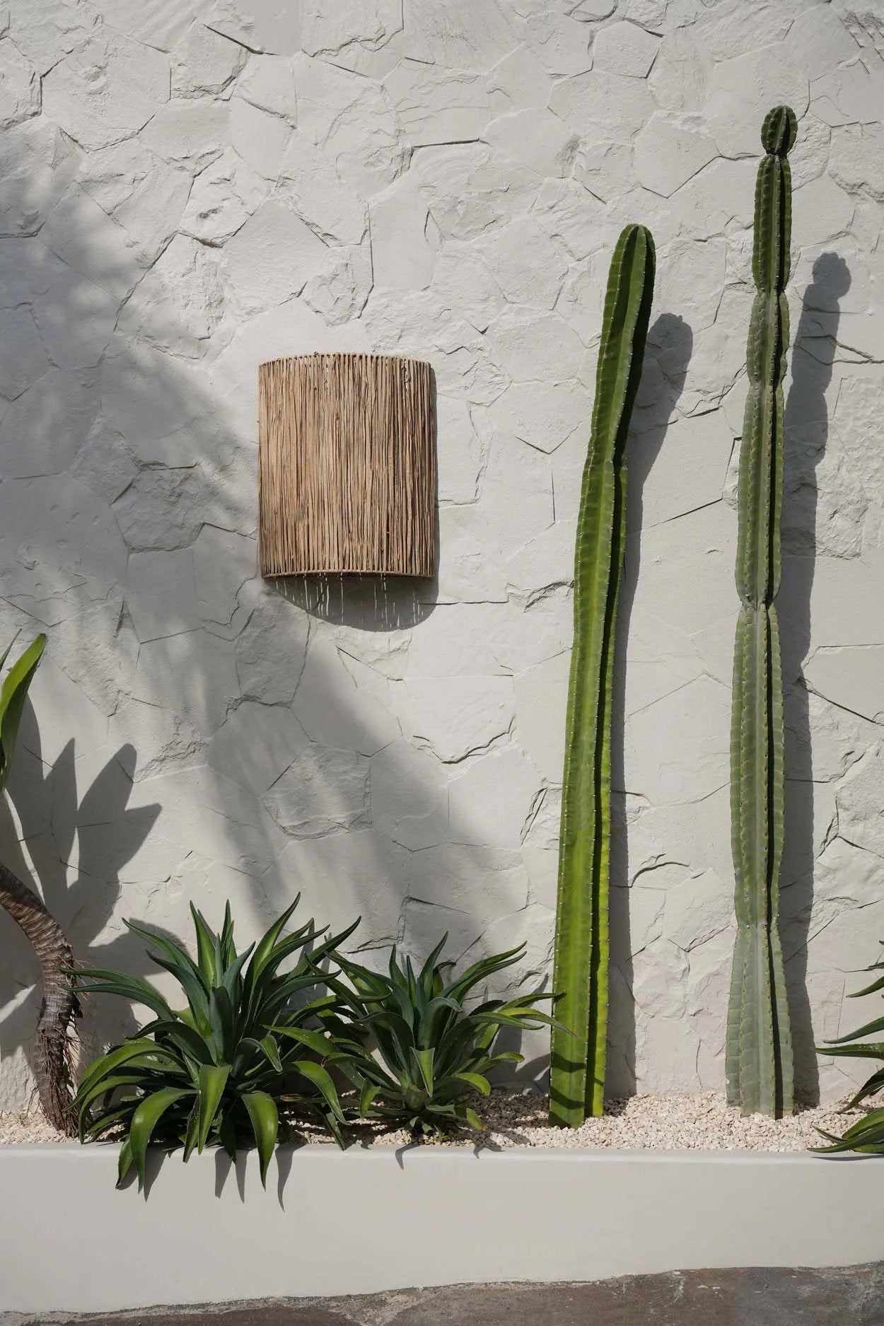 The Kohei Wall Applique shown mounted on an outdoor wall, featuring layered natural fibers that create a warm, inviting glow.