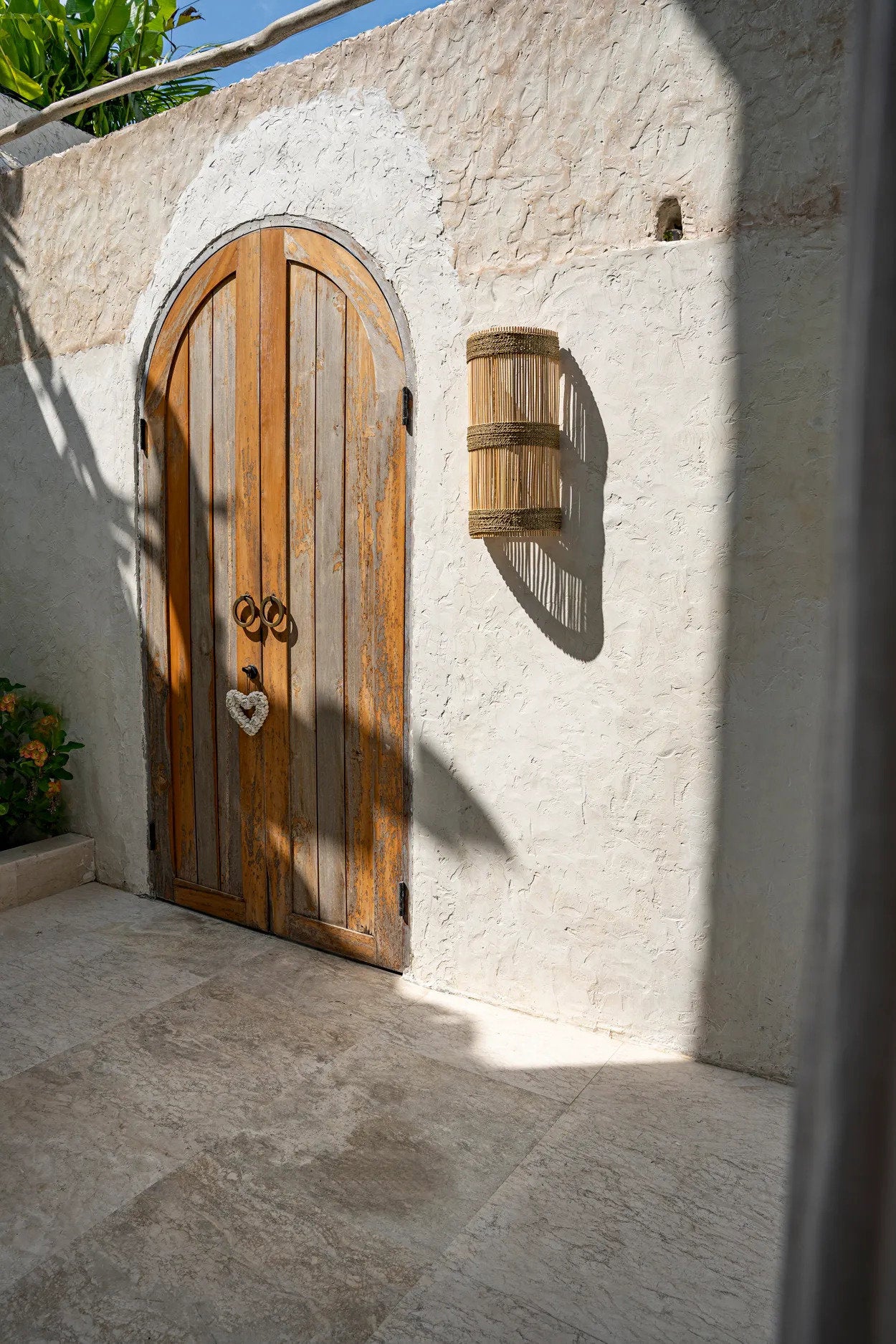 The Jalal Wall Applique in medium size, crafted from durable rattan and mounted in an entryway to provide soft, welcoming light.