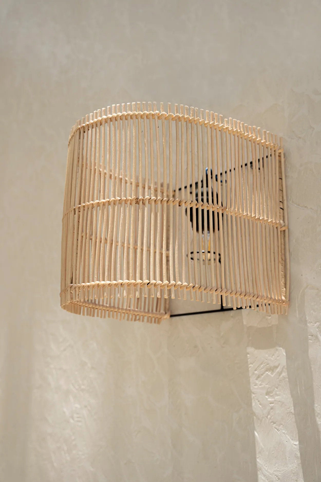 The Gigi Wall Applique in natural rattan, shown mounted on a wall, offering a blend of boho charm and ambient lighting.