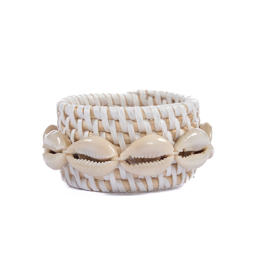 A rounded, white wicker napkin holder, made from rattan and cowrie shells.