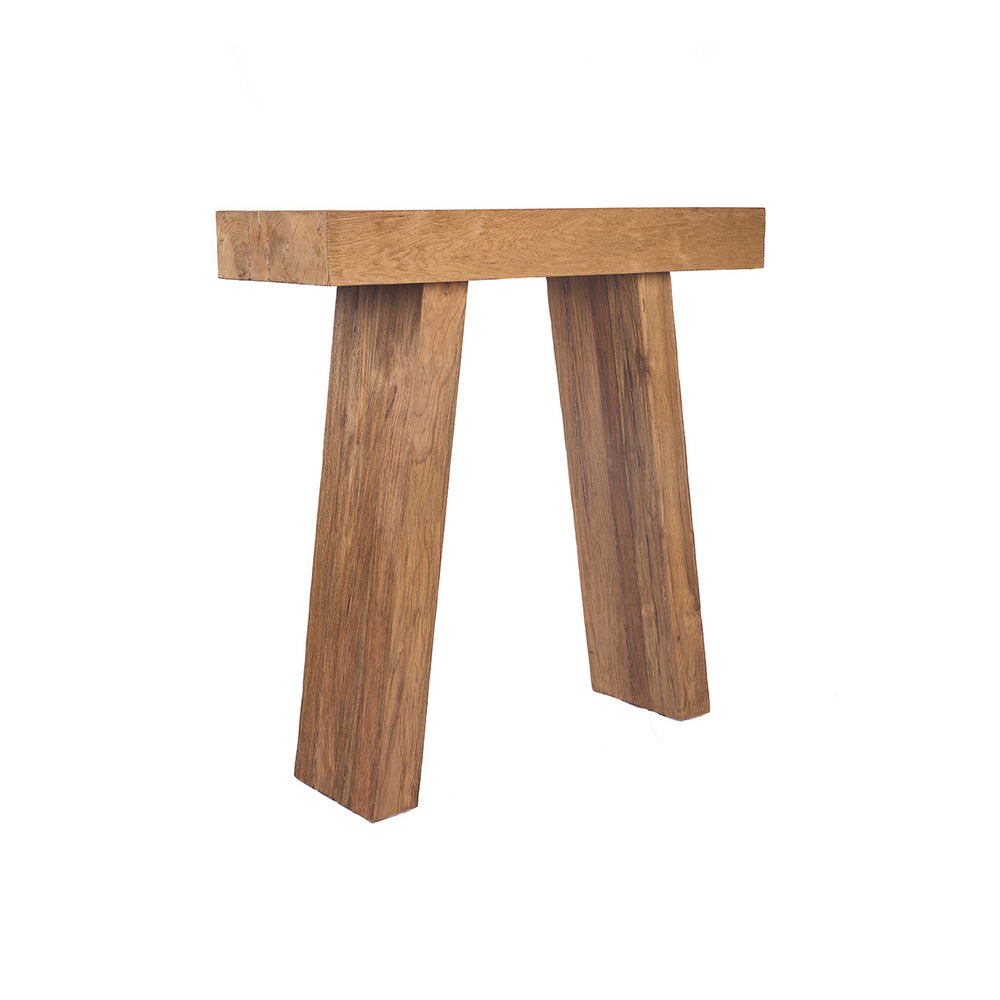 The teak console table stands in natural balance, its warm grain and sculptural lines catching soft light across a calm, minimal space.