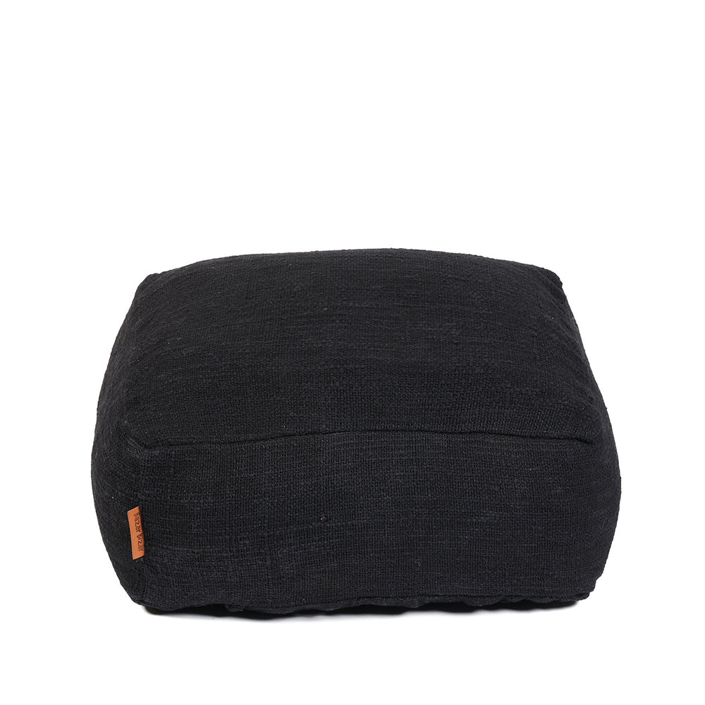 A minimalist black floor pouffe with soft slub-woven texture and a discreet bottom zipper closure.