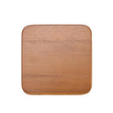 A medium brown wood coaster rests quietly on the table, its smooth teak surface catching soft light and revealing subtle grain and warm, grounded tone.
